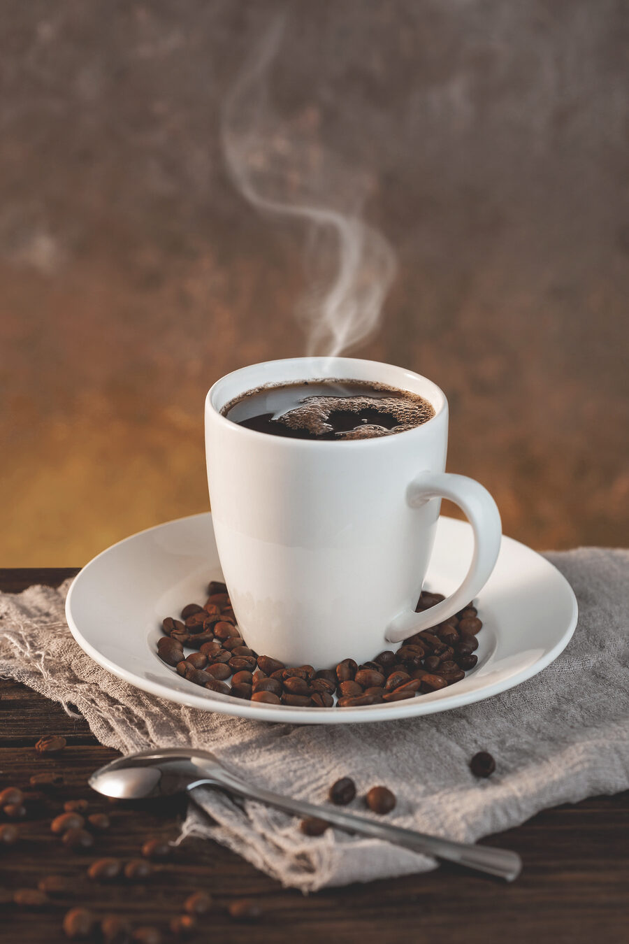 Een kop koffie op een bord met bonen en een lepel