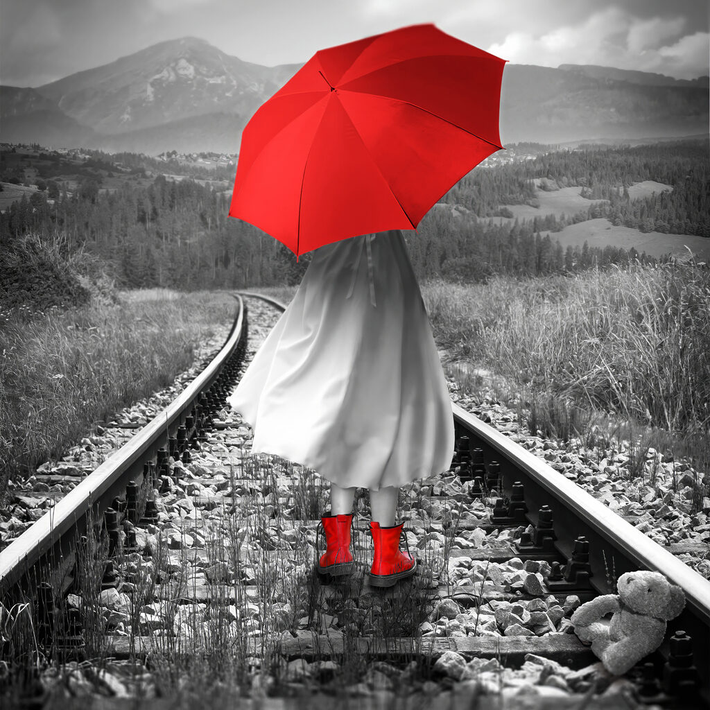 A person with a red umbrella on a train track